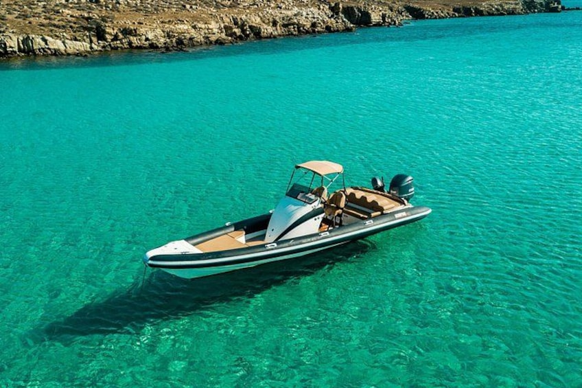 A speedboat on clear turquoise water with rocky coastline in the background. 2
