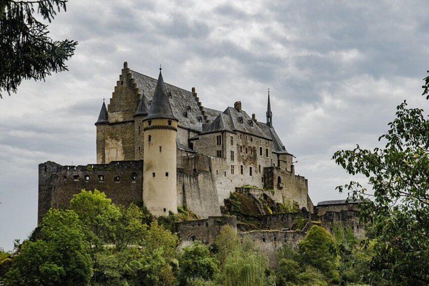 A historic castle with multiple towers and a fortified wall, surrounded by lush greenery. 3