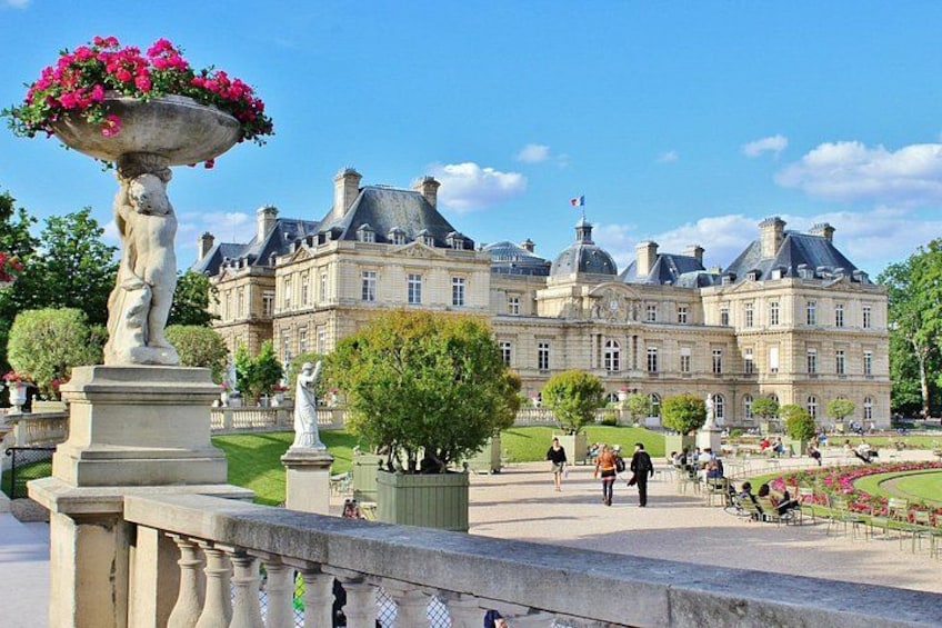 A historic building with a fountain and statues, surrounded by a well-maintained garden and a paved walkway. 2
