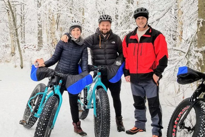 Three people standing next to bicycles in a snowy forest. 1