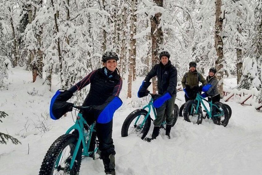 Four people on mountain bikes in a snowy forest. 5