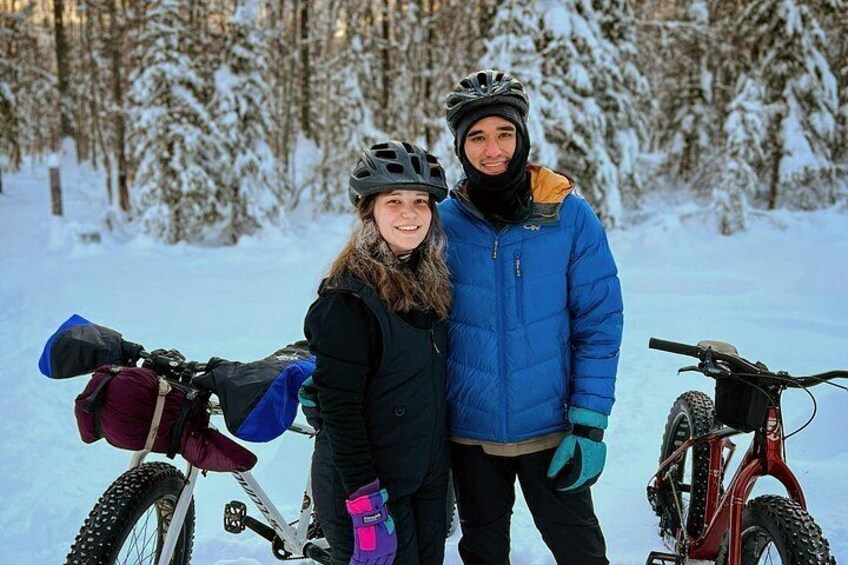 To personer står ved siden af en cykel i en snefyldt skov. 5