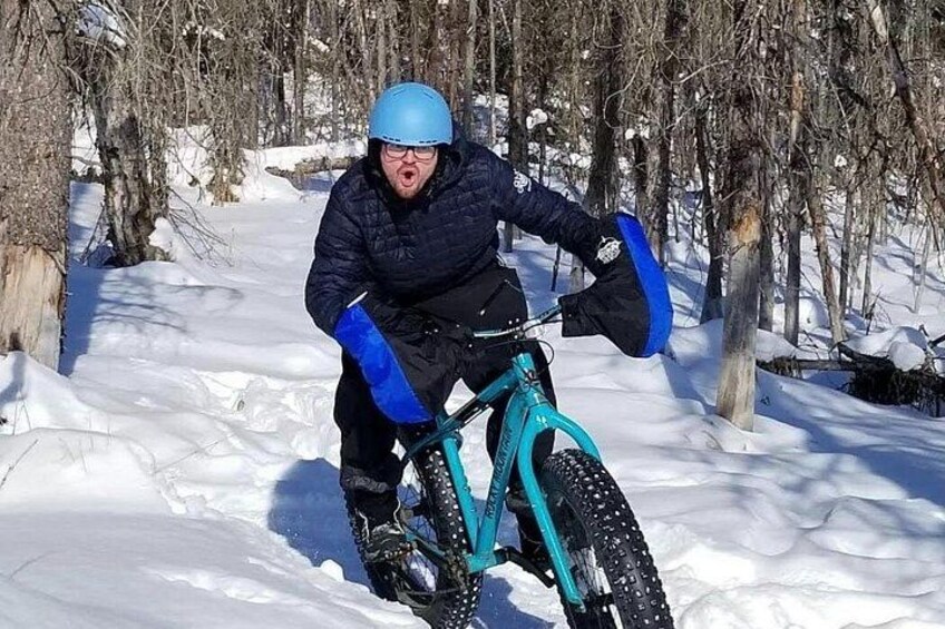A person riding a teal snow bike in a snowy forest. 4