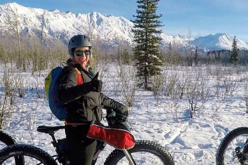 En person cykler på mountainbike i et sneklædt landskab med snefyldte bjerge i baggrunden. 2