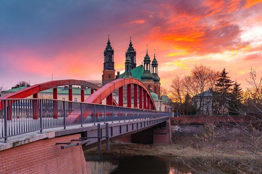 Un ponte ad arco rosso sopra un fiume, una chiesa con cupole verdi e un cielo al tramonto. 1
