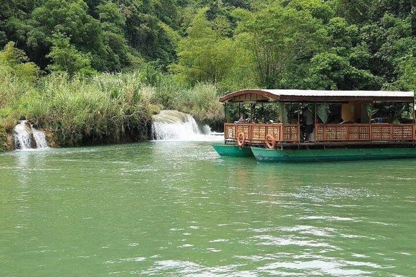 A boat with a covered deck, a waterfall in the background, and lush greenery along the riverbank. 4