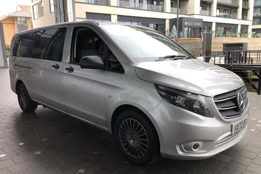 A silver Mercedes-Benz minivan parked on a paved surface with a building in the background. 2