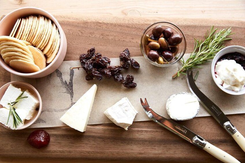 A wooden table with cheese, crackers, olives, dried fruits, and a knife. 2