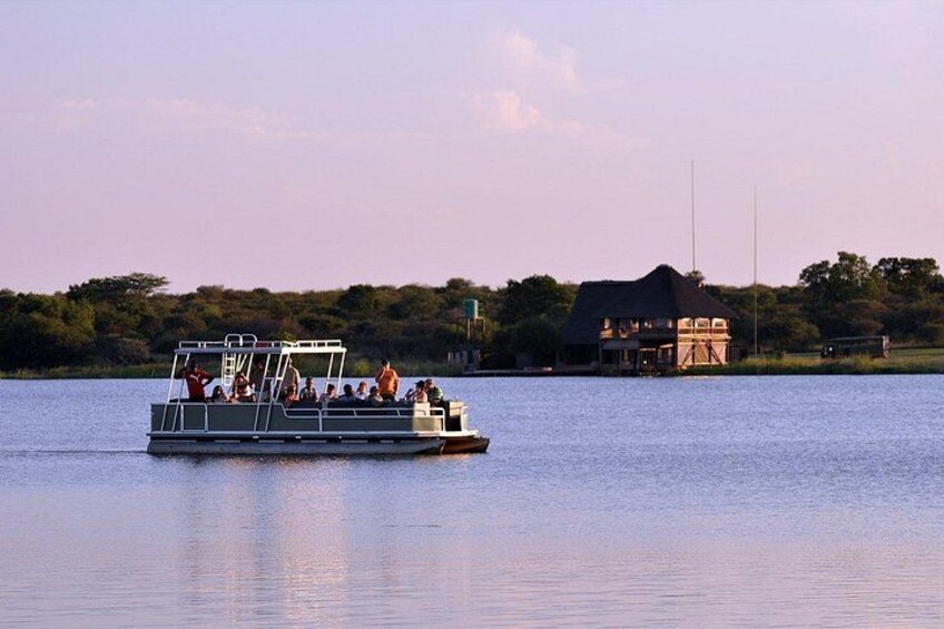 A boat with passengers on a calm body of water, a house in the background, and a clear sky. 2
