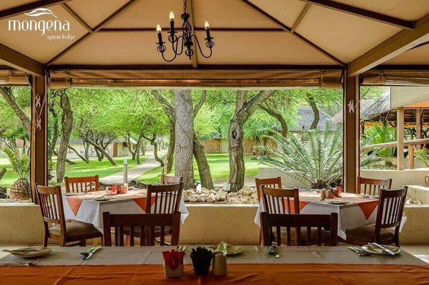 An outdoor dining area with tables and chairs, surrounded by trees and a view of a garden. 5