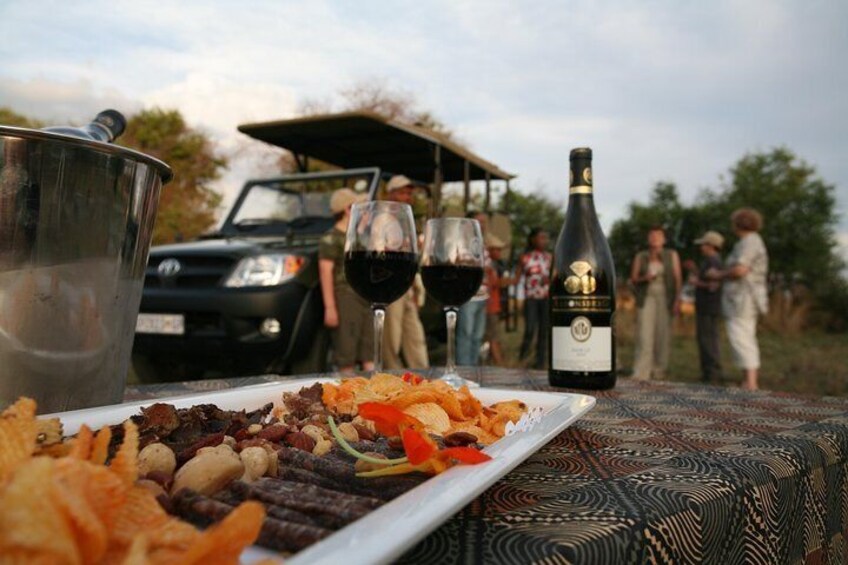 A picnic setup with food, wine, and a vehicle in the background. 1