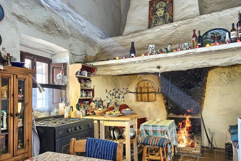Une cuisine rustique avec un poêle à bois, des étagères remplies de bouteilles et une table recouverte d’une nappe à rayures. 1