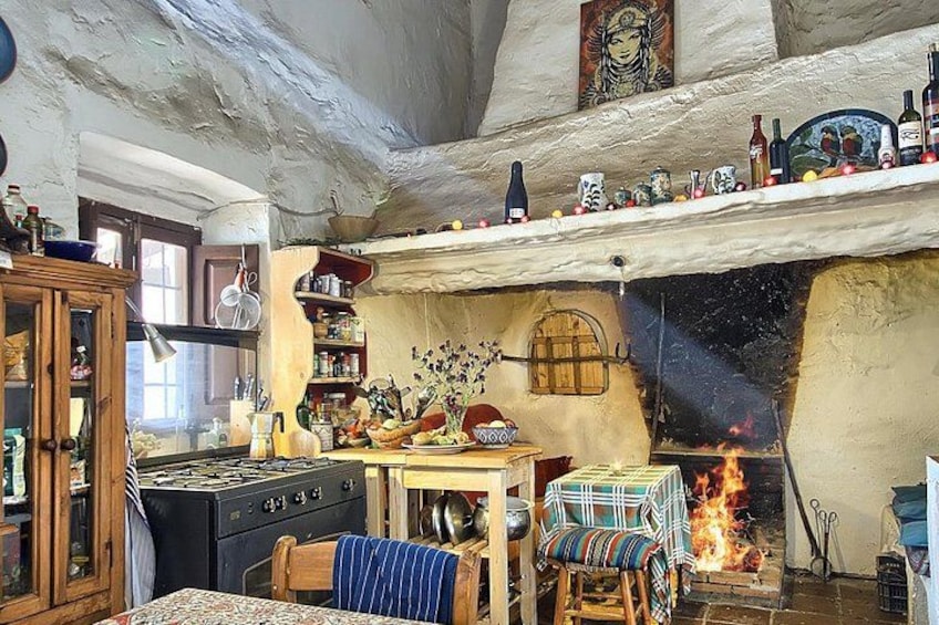 Una cucina rustica con un camino a legna, scaffali con bottiglie e un tavolo con tovaglia a righe. 1