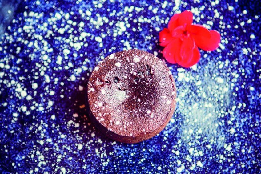 Un gâteau au chocolat rond, saupoudré de sucre glace, posé sur une surface bleue scintillante. 2