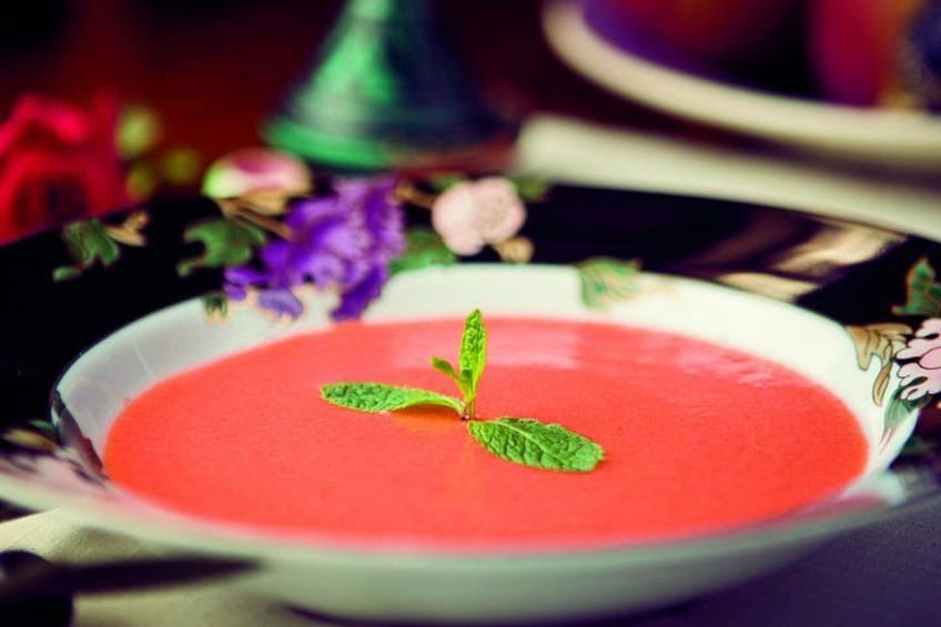 Una ciotola di zuppa rossa guarnita con una foglia di menta, su un piatto decorativo. 5