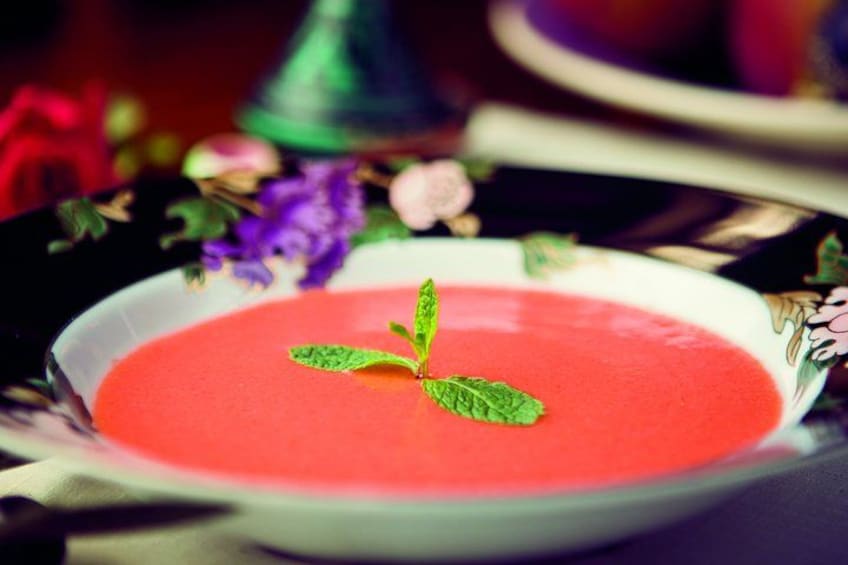 Un bol de soupe rouge, garni d’une feuille de menthe, posé sur une table à motifs floraux. 4