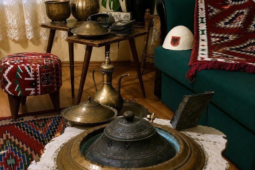 En traditionell miljö med en mässingsfärgad samovar, en mönstrad pall, en vävd matta och en grön soffa med ett dekorativt huvudtyg. 3