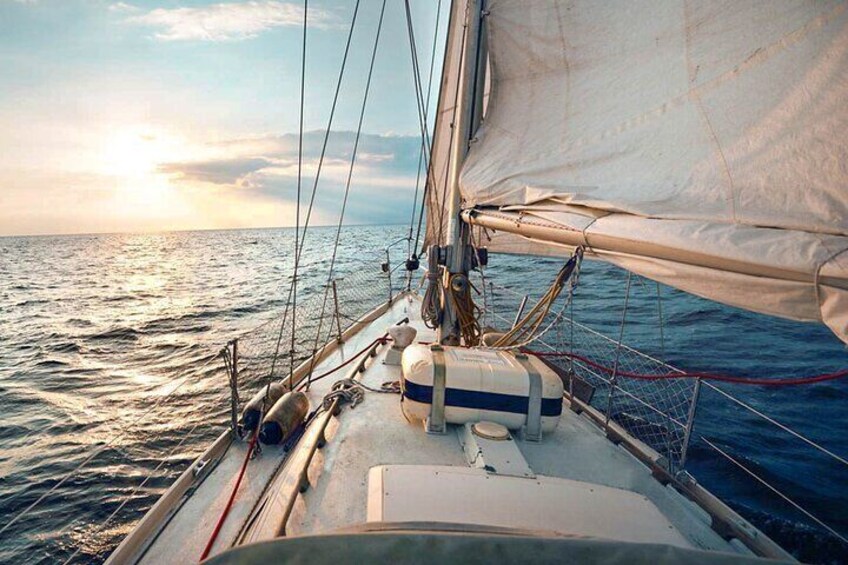 A sailboat with a white sail and a blue stripe, anchored in calm waters with a sunset in the background. 1