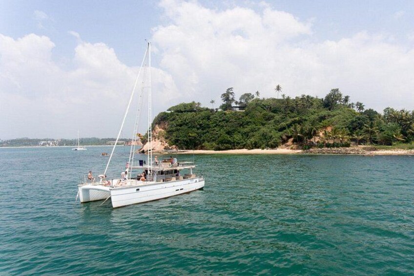A white sailboat on calm waters with a beach and dense foliage in the background. 4