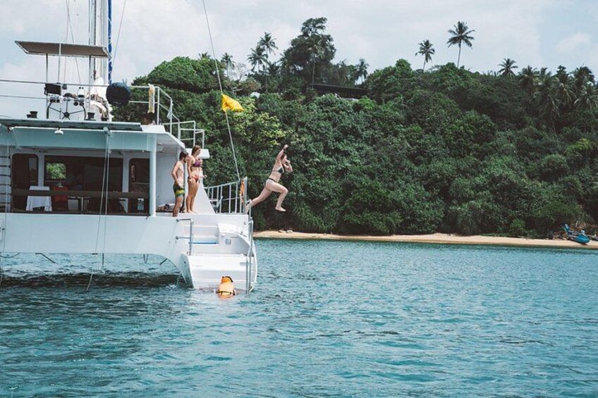 A boat with people on deck, a person jumping into the water, and a beach with palm trees in the background. 2