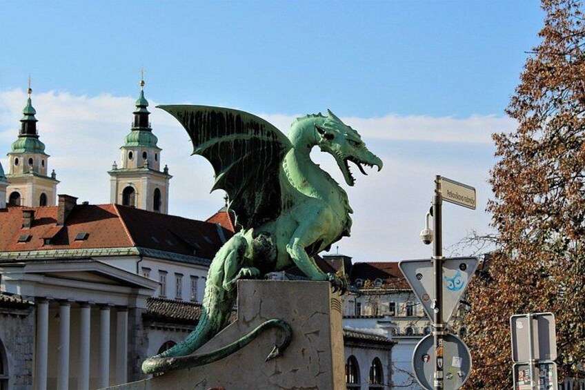 En grön drakstaty på en piedestal, med byggnader och en kyrka i bakgrunden. 1