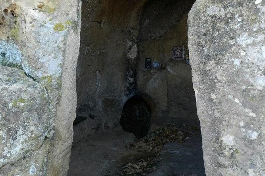 An ancient stone structure with a circular opening, possibly a well or a tomb entrance, surrounded by rough stone walls. 2