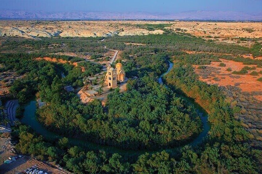 A river winding through a forested area with a church and a hill in the background. 1
