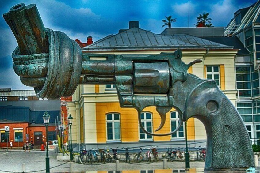 Une grande sculpture métallique, ayant la forme d’un revolver, se trouve devant un bâtiment jaune, à côté d’un espace réservé au stationnement des vélos. 3