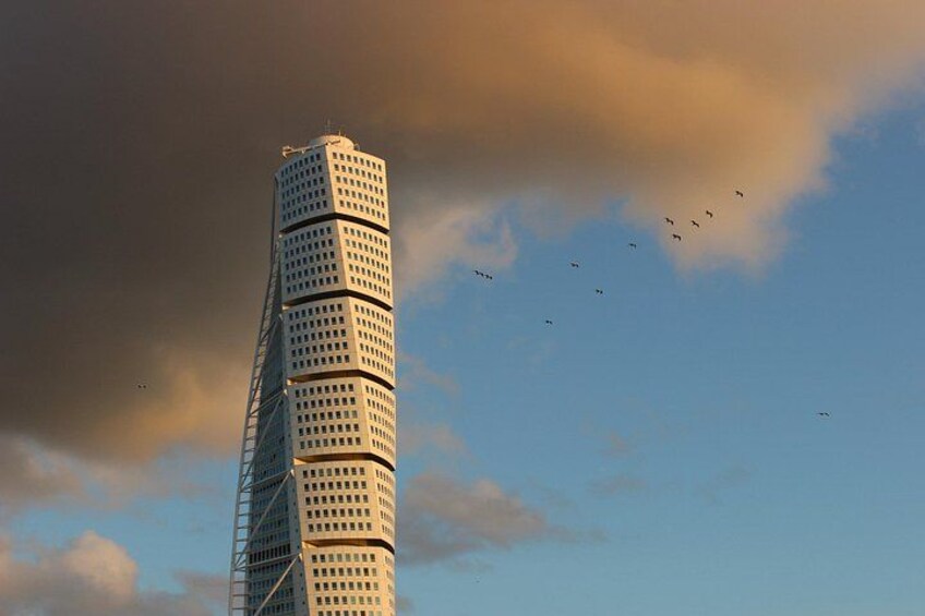 A tall, twisted skyscraper with a grid of windows against a partly cloudy sky. 3