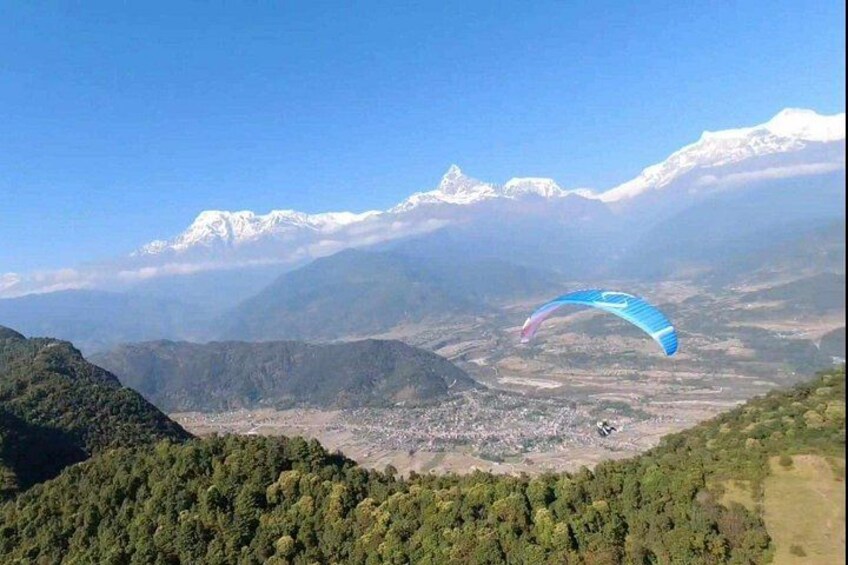 Un parapentista volando sobre un paisaje montañoso con picos nevados al fondo. 1