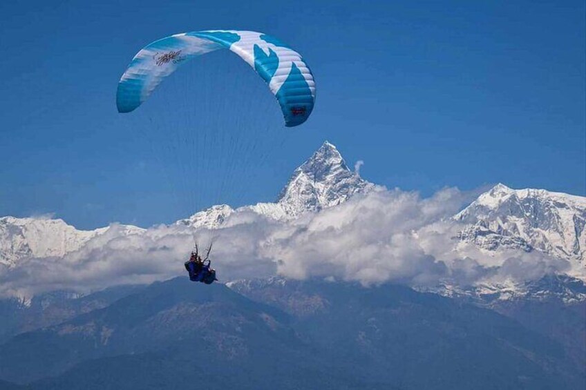 Un parapentista vuela sobre montañas nevadas con un cielo azul despejado. 3