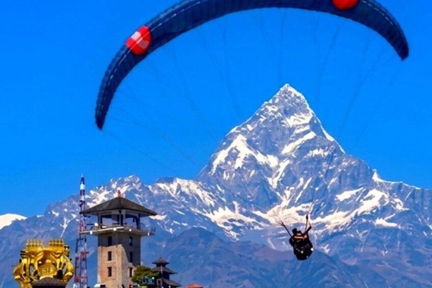 A paraglider flying over a snow-capped mountain with a temple in the foreground. 5