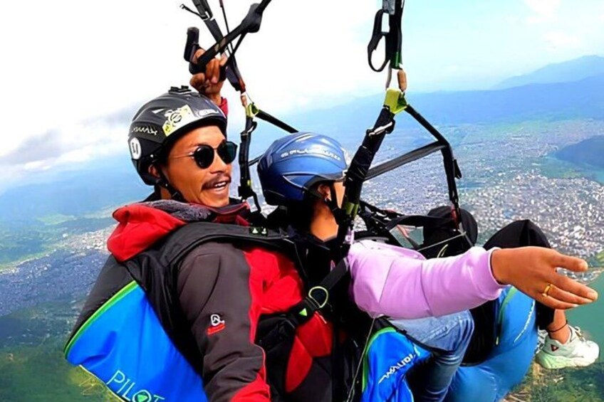 Two people in a tandem paragliding harness with a cityscape in the background. 1