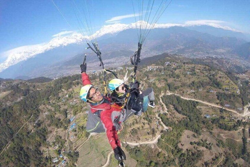 Dos parapentistas con arneses rojo y azul volando sobre un paisaje montañoso con picos nevados al fondo. 4
