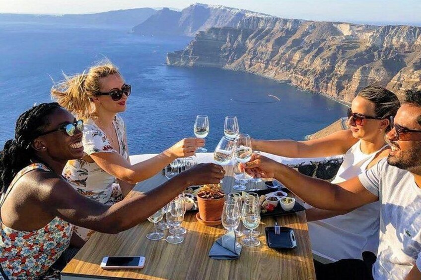 En gruppe mennesker skåler med vinglas ved et bord med udsigt til havet. 4