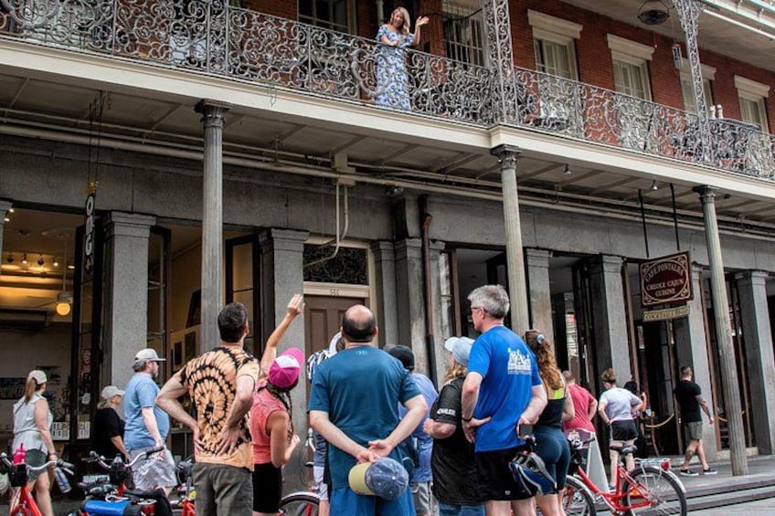 A group of people gathered outside a building with a balcony, some holding bicycles. 3