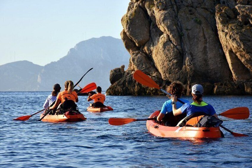 People kayaking on a calm sea with rocky cliffs in the background. 2