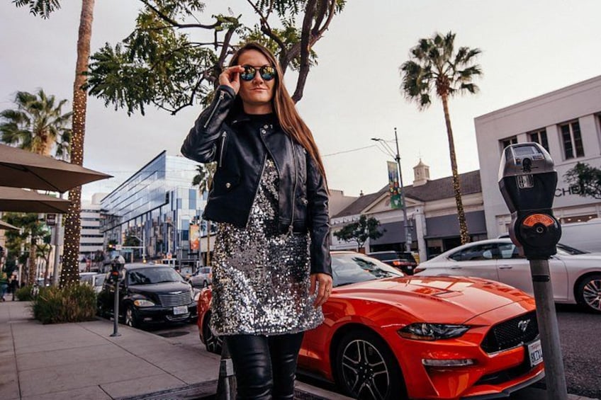 A person standing next to a red sports car, palm trees, and a parking meter. 4