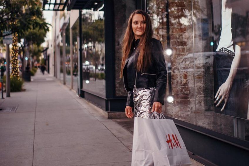 A person walking on a sidewalk, holding a shopping bag with a store logo. 3