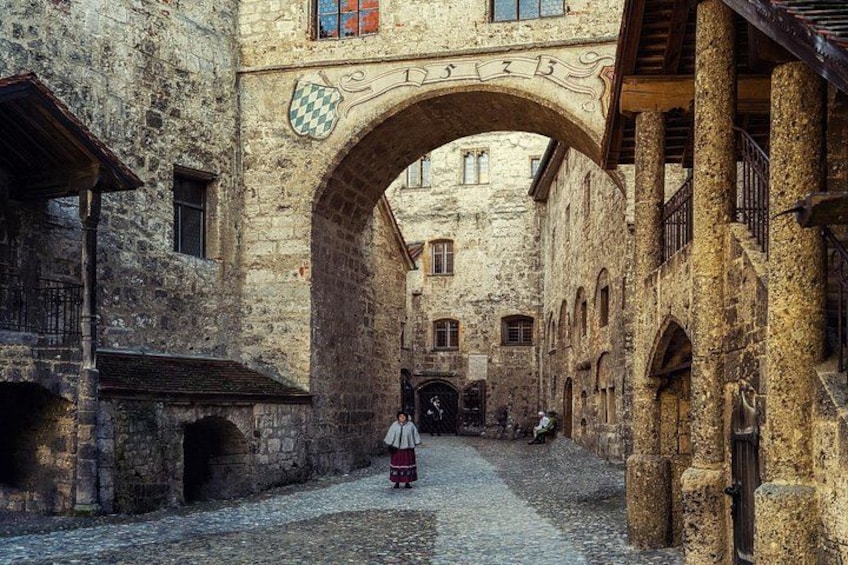 A cobblestone street with an arched gateway, historic buildings, and a person in traditional attire. 4