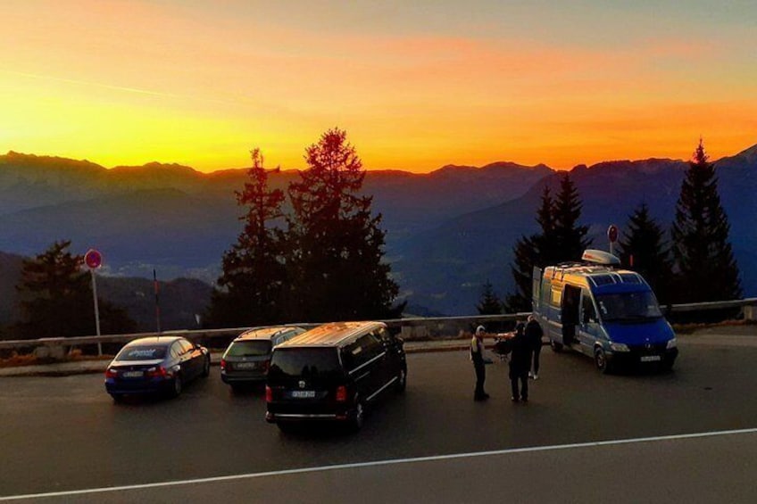 Atardecer con montañas al fondo, una carretera con autos estacionados y una furgoneta, y una señal de no transito. 2