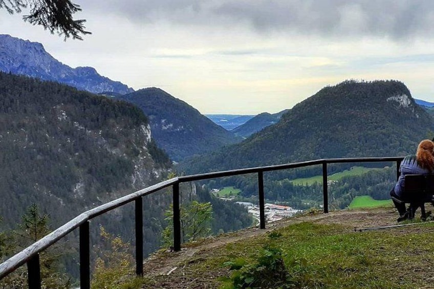 A person sitting on a railing overlooking a valley with mountains in the background. 2
