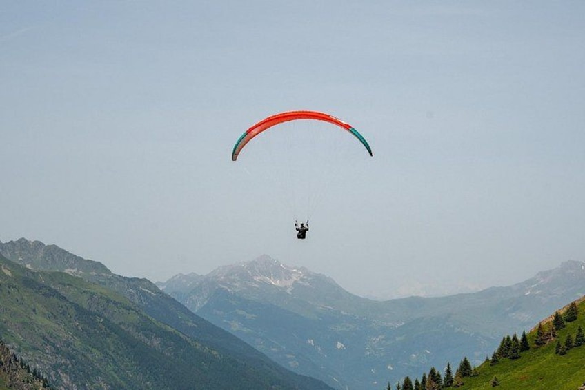 A paraglider in mid-flight over a mountainous landscape. 2