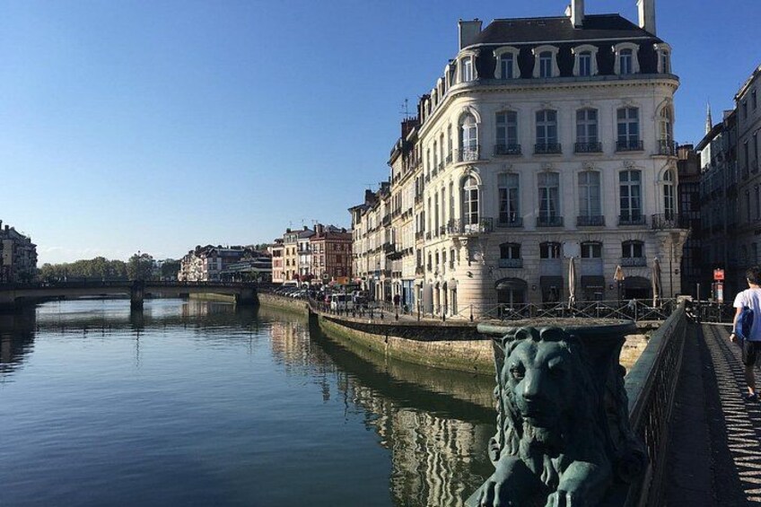 Een rustige rivier met een stenen leeuwenbeeld, een brug en historische gebouwen langs de oever. 3