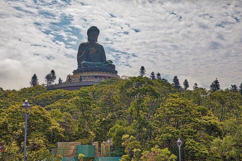 Un'imponente statua di Buddha su una collina, circondata da alberi e con un cielo nuvoloso. 1