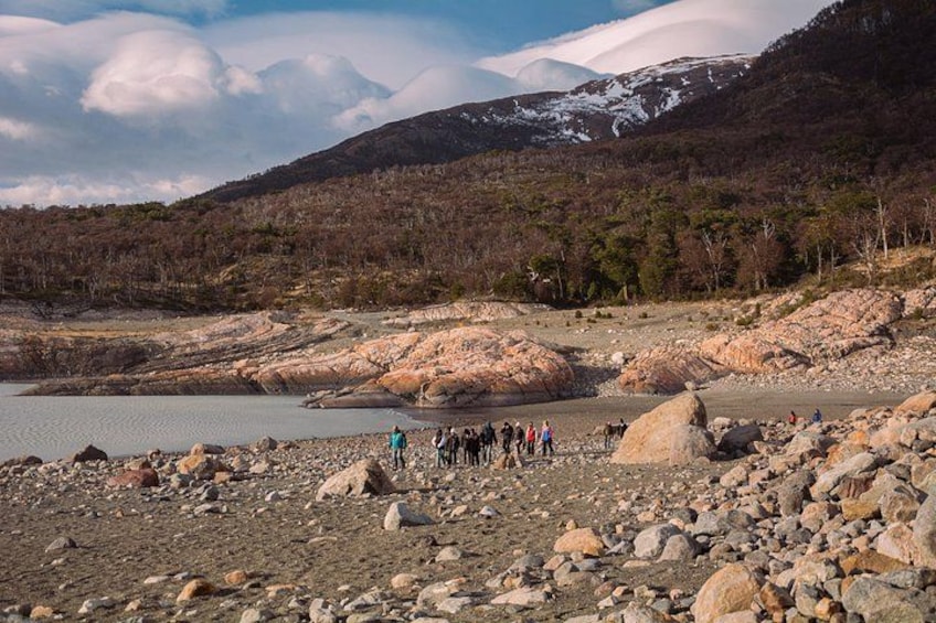 A rocky landscape with a group of people, a lake, and snow-capped mountains in the background. 2