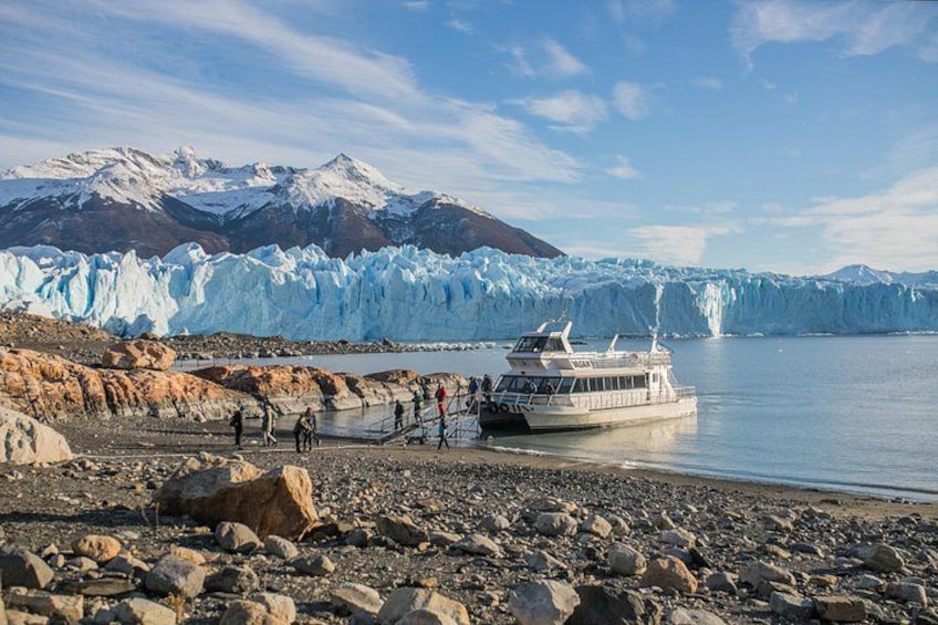 A glacier, a boat, and people on a rocky shore. 5