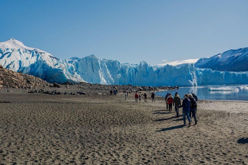 A glacier with people walking on a rocky beach. 3