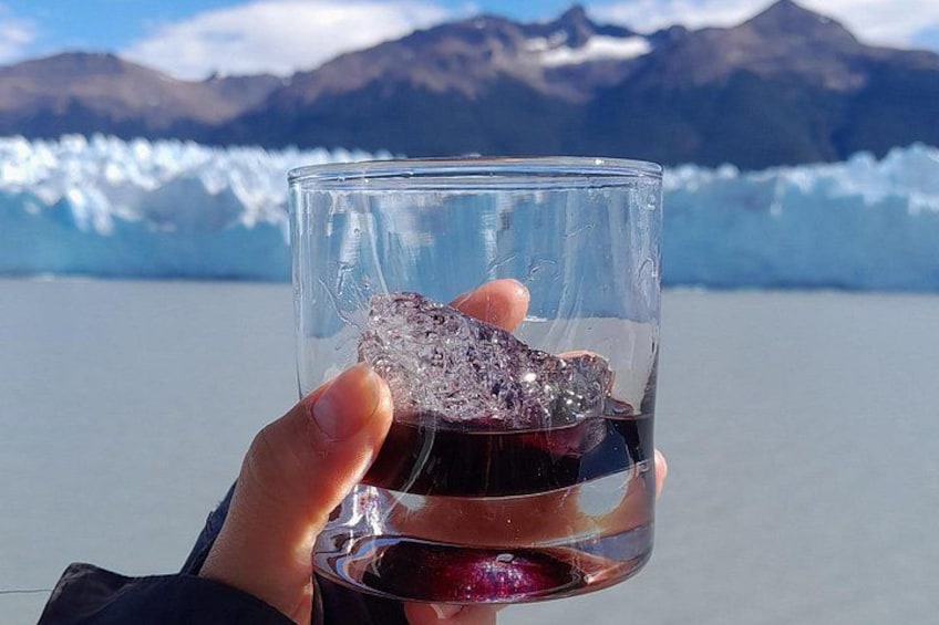 A hand holding a glass with a dark liquid and ice cubes, with a glacier and mountains in the background. 4