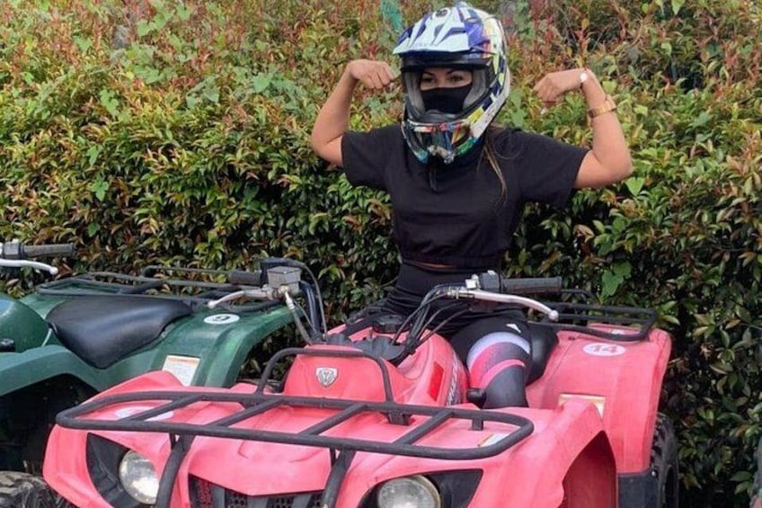 A person sitting on a pink ATV with a green ATV parked beside it, wearing a helmet. 3